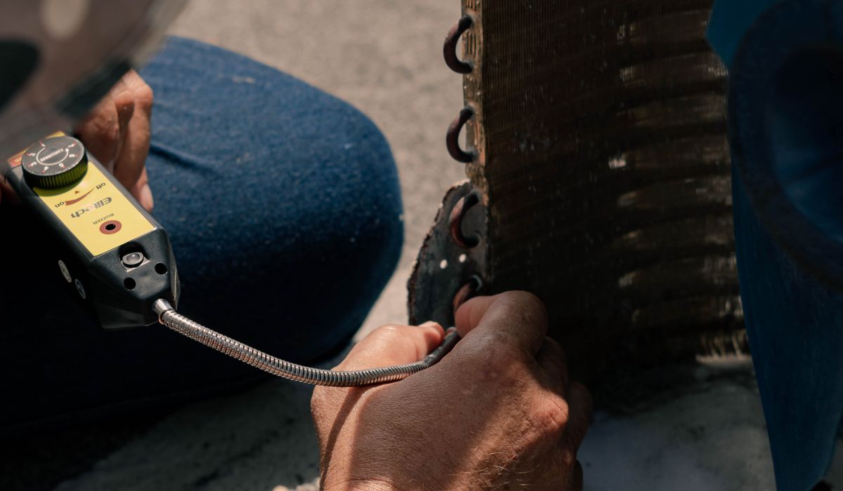 Technician running an electronic leak detector along a condenser coil
