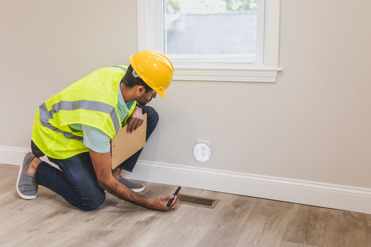 Inspector checking airflow at a floor supply vent inside a home